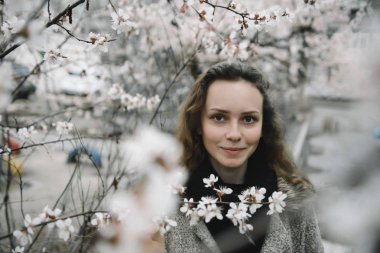 Çiçekli bir ağaca karşı sokakta poz veren genç bir kadın.