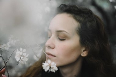 Çiçekli bir ağaca karşı sokakta poz veren genç bir kadın.