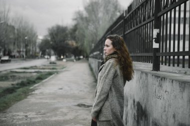 Kahverengi hırkayla sokakta poz veren genç bir kadın.