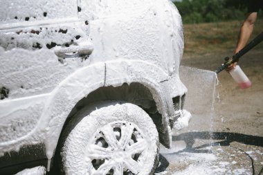 Bir adam, arabaya yüksek basınç uygulayan bir temizlik maddesini püskürtüyor.