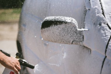 Bir adam, arabaya yüksek basınç uygulayan bir temizlik maddesini püskürtüyor.