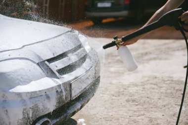 Bir adam, arabaya yüksek basınç uygulayan bir temizlik maddesini püskürtüyor.