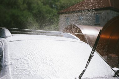 Bir adam, arabaya yüksek basınç uygulayan bir temizlik maddesini püskürtüyor.