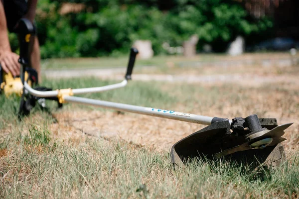 Gardener mows the grass with a trimmer in the yard in the summer. — Stock Photo, Image