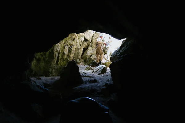 Dark cave with a bright daylight spot of exit. Natural cave opening. Entrance to the karst cave in a mountain.