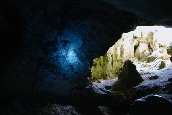 Dark cave with a bright daylight spot of exit. Natural cave opening. Entrance to the karst cave in a mountain.