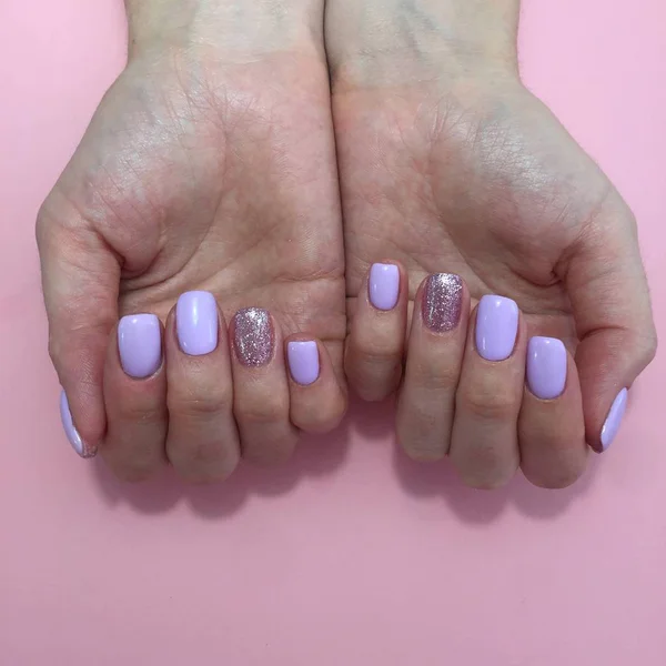 Manicure van verschillende kleuren op nagels. Vrouwelijke manicure op de hand op een roze achtergrond — Stockfoto