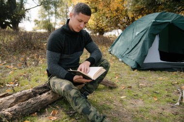 Ormandaki çadırın yanında bir adam deftere yazıyor.