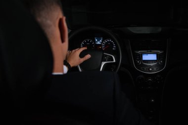 Takım elbiseli adam içeriden bir arabanın arkasında oturuyor.