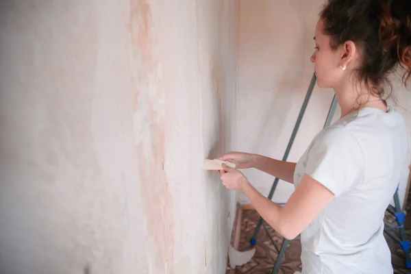 Home renovation, room wall repairing, woman removing old wallpaper