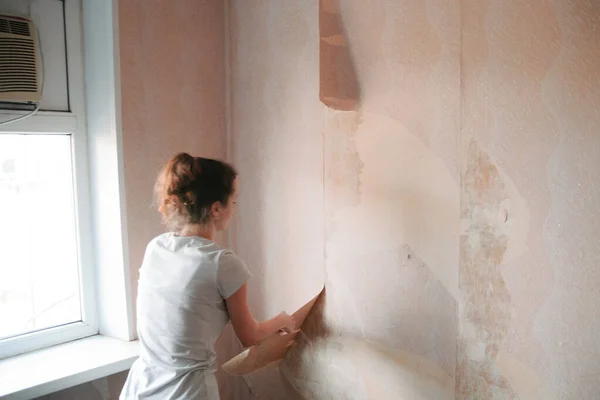 Home renovation, room wall repairing, woman removing old wallpaper