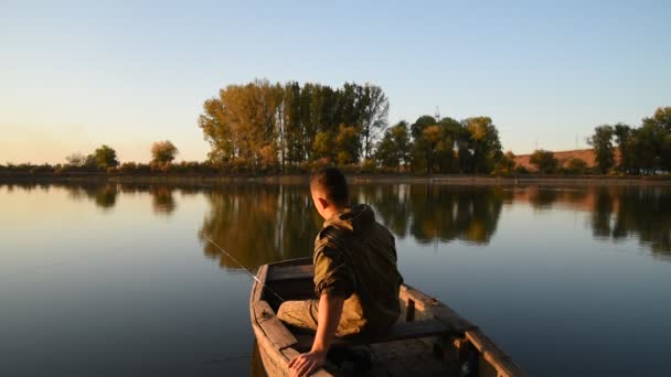 A young man catches fish on the river bank at sunset. A fisherman catches fish at sunset on the river bank — Stock Footage Young Man Catches Fish River Bank Sunset Fisherman Catches Fish Royalty Free Stock Video