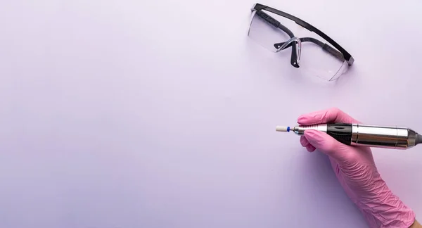 Nail drill. A manicurist in gloves holds a nail drill on white bacground