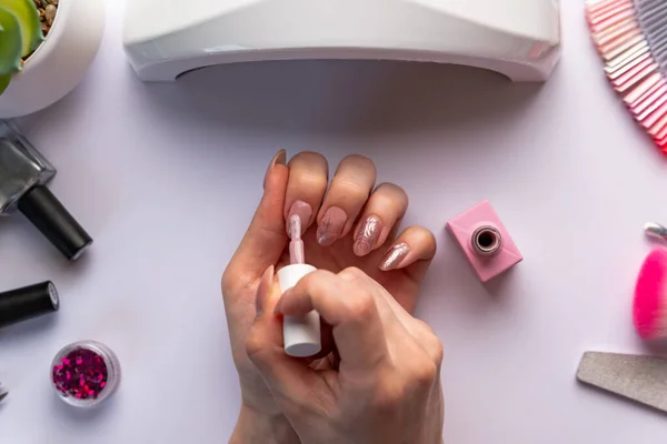 Woman giving herself manicure on white background. Concept of nail art. Woman gives herself a manicure on a white table