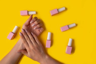Pembe renkli jöle cilası ve sarı arka planda manikürlü eller, üst manzara. Sarı arka planda kadın eli ve pembe cila şişesi. Manikür kavramı