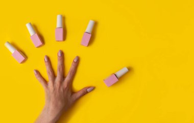 Pembe renkli jöle cilası ve sarı arka planda manikürlü eller, üst manzara. Sarı arka planda kadın eli ve pembe cila şişesi. Manikür konsepti, afiş