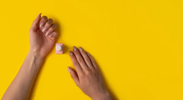 Gel polish of pink color and hands with manicure on a yellow background, top view. Woman hands and pink bottle of varnish on a yellow background. Manicure concept,banner