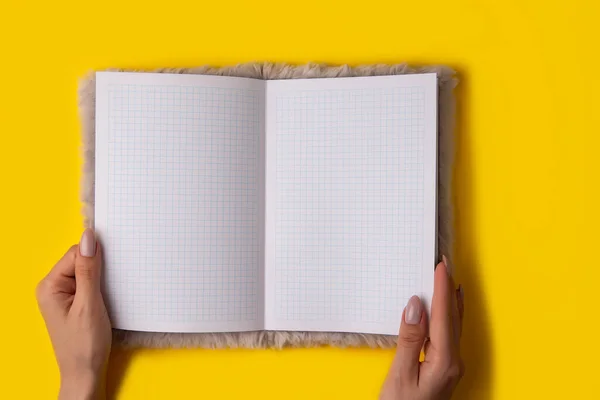 黄色の背景に手のノートブックの空の広がりを保持し トップビュー 女性保持していますオープン空白のノートブックで彼女の手 — ストック写真