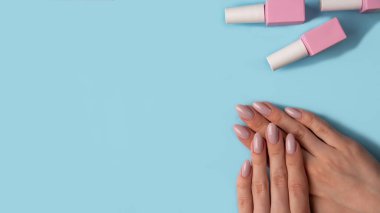 Güzel manikürlü kadın elleri ve mavi arka planda pembe jel cilası olan şişeler, üst manzara, düz yatak. Manikür konsepti, afiş