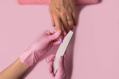 Manikür süreci, en iyi görüntü. Güzellik salonunda manikür. Manikür konsepti, düz yatak. Manikürcü tırnak törpüsü kullanıyor. Kostüm sahibinin tırnakları üzerine seçici odak.