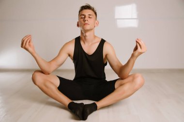 Spor elbiseli genç adam evde yoga yaparken Lotus pozisyonunda meditasyon yapıyor. Evdeki karantinada. Online dersler. Akıllı telefondaki bir uygulama ile çalışma