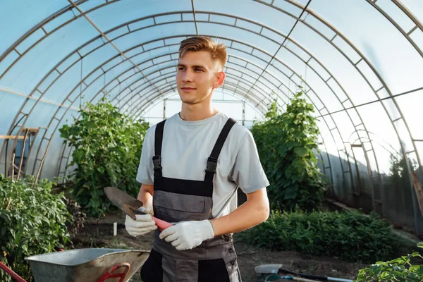 Man with garden tools.Young happy farmer posing with abrasive tools in a greenhouse.Man posing with garden tools.Gardening, Farming and Agriculture Concept