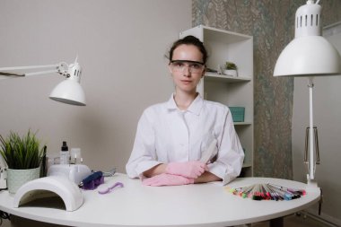 Güzellik salonundaki güzel manikürcü kız. Manikür, pedikür ve güzellik konsepti. Manikürcü, manikür salonundaki bir iş yerinde oturuyor.