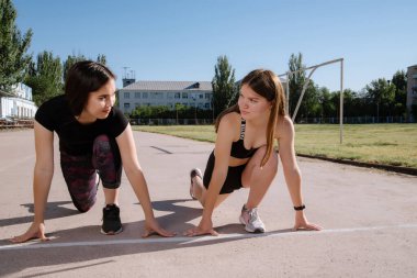 Stadyumdaki başlangıç pozisyonunda iki atlet. Atletik kızlar stadyumda koşuyor. Kızlar egzersiz yapıyor, esniyorlar. Spor ve sağlıklı yaşam tarzı.