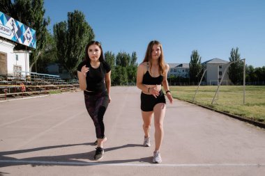 Stadyumdaki başlangıç pozisyonunda iki atlet. Atletik kızlar stadyumda koşuyor. Kızlar egzersiz yapıyor, esniyorlar. Spor ve sağlıklı yaşam tarzı.