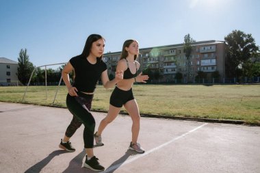 Stadyumdaki başlangıç pozisyonunda iki atlet. Atletik kızlar stadyumda koşuyor. Kızlar egzersiz yapıyor, esniyorlar. Spor ve sağlıklı yaşam tarzı.
