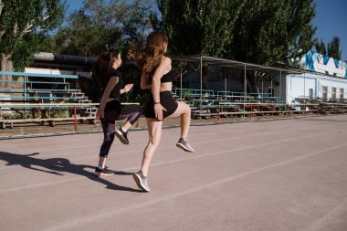 Atletik kızlar koşuyor, atletik kızlar stadyumda koşuyor. Genç kadınlar güneşli bir sabahta stadyumda koşuyor. Kızlar egzersiz yapıyor, esneme hareketleri yapıyor. Spor ve sağlıklı yaşam tarzı.