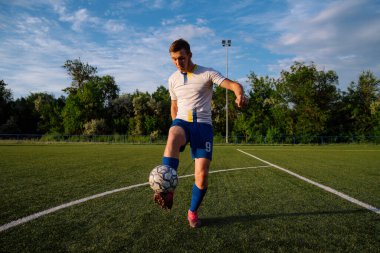Genç erkek futbolcu futbol sahasında top çeviriyor. Stadyumda ayaklarıyla top hokkabazlığı yapıyor. Futbol sporu konsepti.