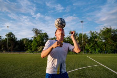 Genç erkek futbolcu futbol sahasında top çeviriyor. Spor, futbol ve diğer insanlar - futbol oyuncusu sahada başlık tekniğini kullanarak top oynuyor ve hokkabazlık yapıyor. Futbol sporu kavramı.
