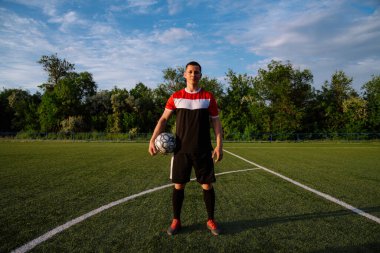 Elinde top olan bir futbolcu. Futbol sahasında elinde futbol topu tutan genç bir futbolcunun portresi. Futbol sporu konsepti.