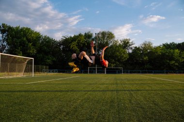 Futbolcu bir futbol stadyumunda gol kutluyor. Futbolcu ters takla atıyor. Mutlu futbolcu bir futbol stadyumunda zaferi kutluyor.