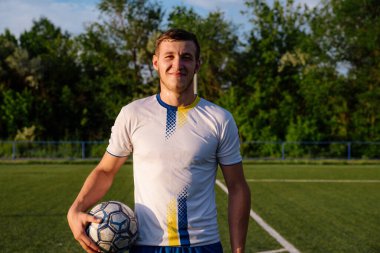 Elinde top olan bir futbolcu. Futbol sahasında elinde futbol topu tutan genç bir futbolcunun portresi. Futbol sporu konsepti.