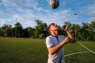 Genç erkek futbolcu futbol sahasında top çeviriyor. Spor, futbol ve diğer insanlar - futbol oyuncusu sahada başlık tekniğini kullanarak top oynuyor ve hokkabazlık yapıyor. Futbol sporu kavramı.