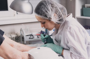 Güzellik salonunda profesyonel pedikür yaptıran genç bir kadın. Pedikür uzmanı ayak tırnaklarını jöle cilası ile boyuyor. Pedikür yaparken ustalaşıyor. Profesyonel pedikür süreci.