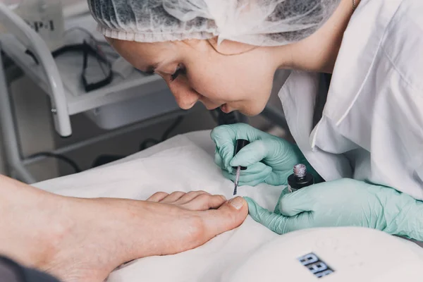 Young woman getting professional pedicure in beauty salon.Pedicure master paints toenails with gel polish.Master during a pedicure. The process of professional pedicures.