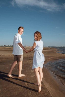 Sahilde aşık bir çift. Kumsalda mutlu genç bir çift. Genç adam ve kadın sahilde yürüyor ve gülüyorlar..