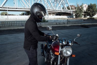 Kasklı motosikletçi motosikleti bir paçavra ile temizler ve motosikletini yıkar.