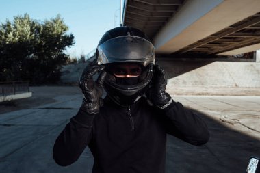 Yakışıklı bir motorcu kaskını takar. Motosikletli bir kask takıyor.