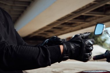 Motosikletçi ellerine siyah deri eldiven takar. Motosiklet sürmeden önce koruyucu eldiven takar.