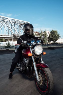 Motosiklette erkek koltuğu. Kasklı adam motosiklette poz veriyor. Siyah kasklı motosikletli adam kırmızı bisikletli.