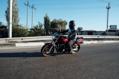 Adam şehirde motosiklet sürüyor. Kasklı ve teçhizatlı genç adam yolda motosiklet sürüyor. Gün boyunca bisiklet sürüyor.