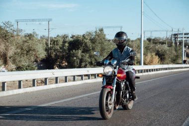 Adam şehirde motosiklet sürüyor. Kasklı ve teçhizatlı genç adam yolda motosiklet sürüyor. Gün boyunca bisiklet sürüyor.