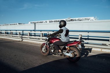 Adam şehirde motosiklet sürüyor. Kasklı ve teçhizatlı genç adam yolda motosiklet sürüyor. Gün boyunca bisiklet sürüyor.