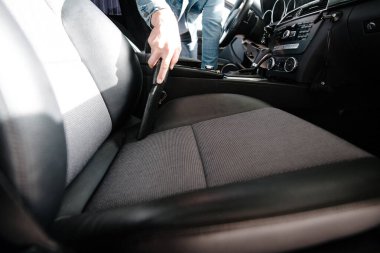 Adam arabanın içini elektrikli süpürgeyle temizliyor. Elektrikli süpürge kullanarak araba temizliyor.