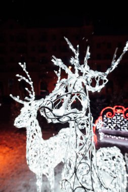 Sokakta Noel süsleri. Beyaz Noel geyiği. Dışarıdaki çelenkler sokağı süslüyor. Noel arifesinde sokakta geyik şeklinde tatil ışıkları..