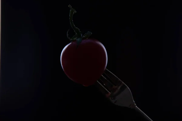 Ripe tomato on the tip of a fork on a black background.